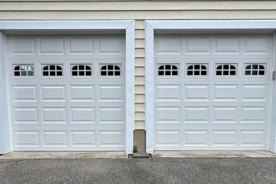 Garage door replacement near me featuring two white paneled doors with decorative windows for homeowners planning garage door replacement, comparing garage door replacement cost, selecting a replacement garage door, or looking to replace garage door systems.