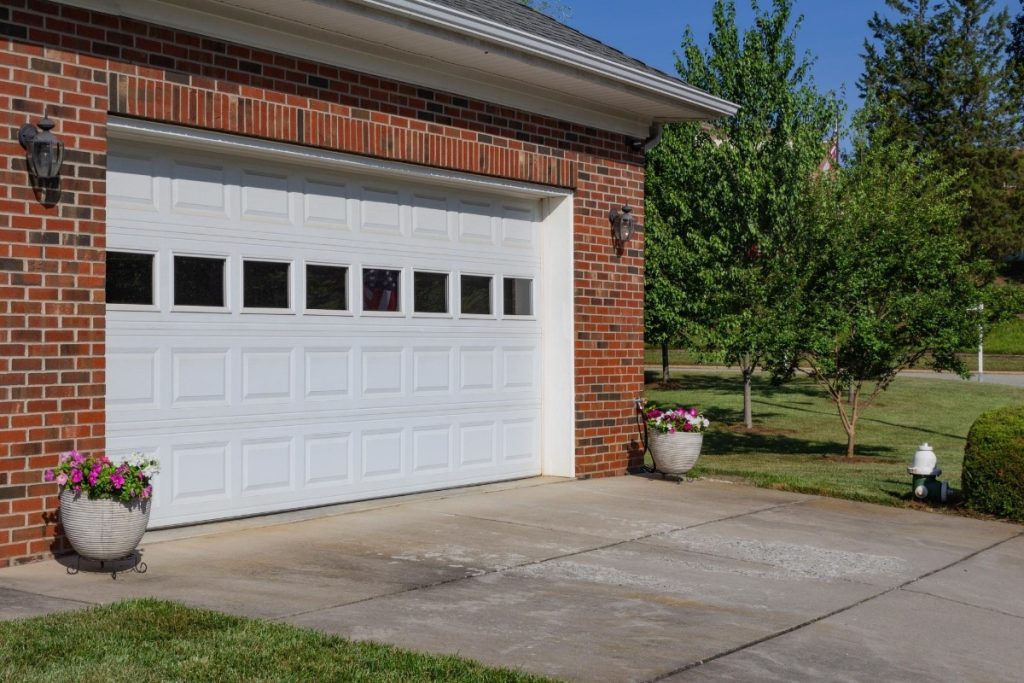 Garage door replacement contractor installing a white paneled door with decorative windows on a brick home for homeowners searching best garage door replacement near me, garage door replace near me, and cost to replace garage door.