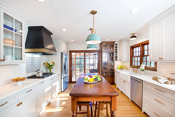 Bright remodeled kitchen by a Kitchen remodeling contractor, featuring white cabinetry, a large wood center island, pendant lighting, hardwood flooring, and updated finishes from a kitchen remodeling company, kitchen remodelers, companies that remodel kitchens, and kitchen renovation contractors.
